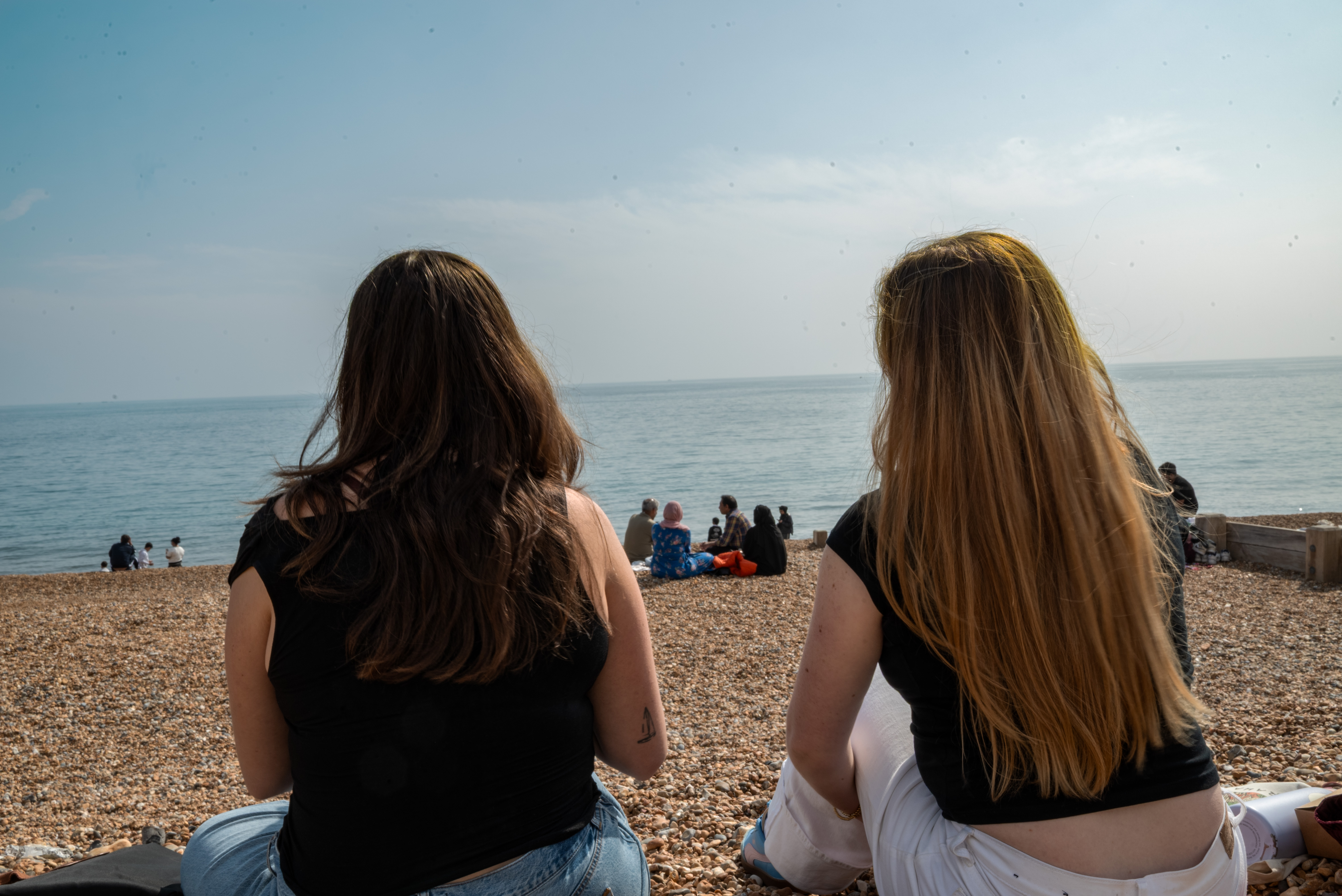 friends: two girls sitting on the beach with their backs turned to the camera
